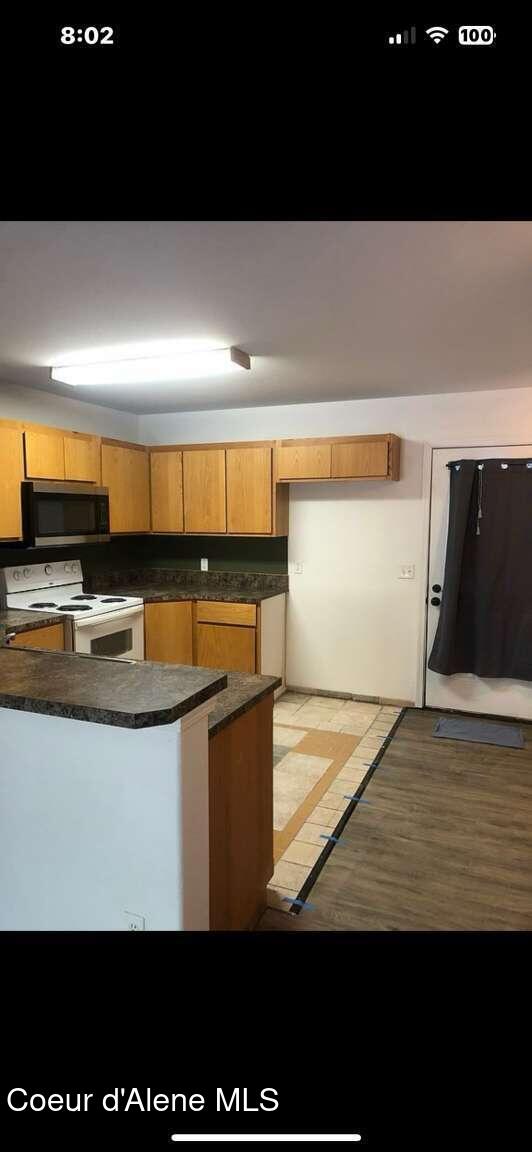 243 Pine St, Moyie Springs, ID 83845 - kitchen featuring stainless steel microwave, white range with electric cooktop, dark countertops, light wood-style floors, and a peninsula