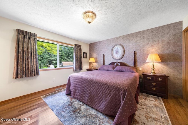 8416 N Haye Ln, Newman Lake, WA 99025 - bedroom with wallpapered walls, baseboards, wood finished floors, a textured ceiling, and an accent wall