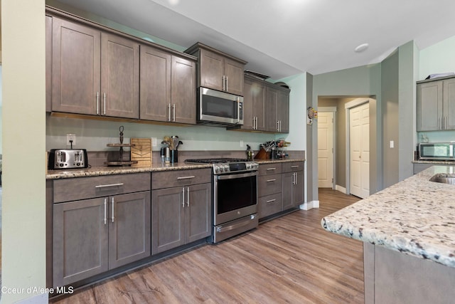 53 Koyokuk Trl, Spirit Lake, ID 83869 - kitchen featuring stainless steel appliances, light wood-type flooring, light stone countertops, dark brown cabinetry, and a sink
