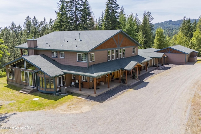 15964 N Songbird Ln, Rathdrum, ID 83858 - rear view of property with a shingled roof, driveway, a view of trees, and a porch