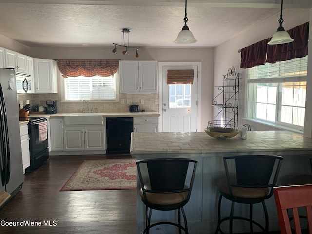 705 S Division St, Kellogg, ID 83837 - kitchen with black appliances, decorative backsplash, a kitchen bar, white cabinetry, and a textured ceiling