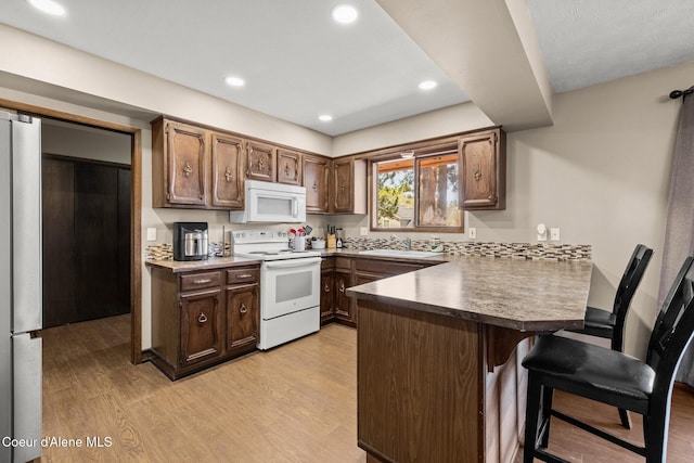 1364 C St, Plummer, ID 83851 - kitchen with white appliances, a peninsula, a kitchen breakfast bar, light wood-style flooring, and recessed lighting