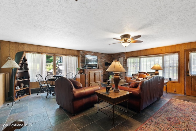 10851 W Pine St, Sandpoint, ID 83864 - living room featuring healthy amount of natural light, wooden walls, a ceiling fan, a textured ceiling, and stone tile flooring