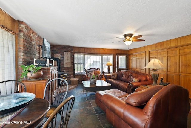 10851 W Pine St, Sandpoint, ID 83864 - living area featuring a wood stove, a ceiling fan, wooden walls, brick wall, and stone finish flooring