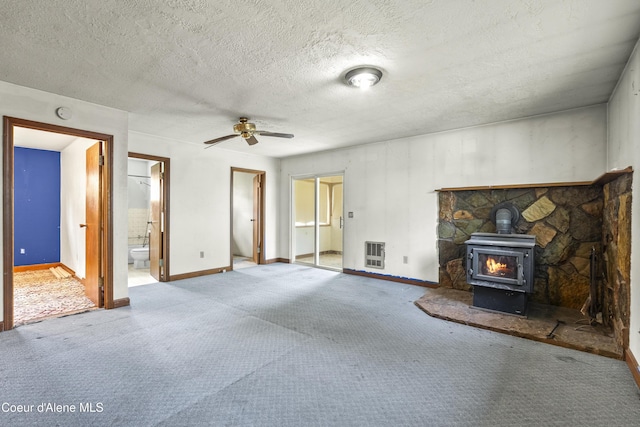 206 E 2nd Ave, Clark Fork, ID 83811 - unfurnished living room with a wood stove, ceiling fan, baseboards, carpet floors, and a textured ceiling