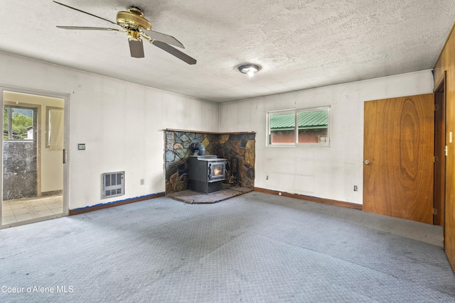 206 E 2nd Ave, Clark Fork, ID 83811 - unfurnished living room with healthy amount of natural light, a wood stove, carpet floors, ceiling fan, and a textured ceiling