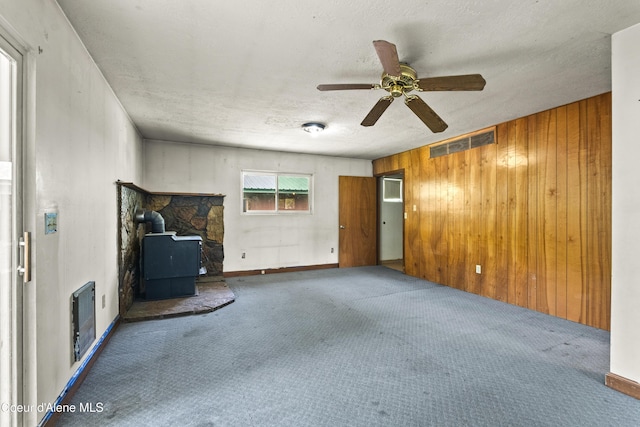 206 E 2nd Ave, Clark Fork, ID 83811 - unfurnished living room featuring a wood stove, carpet flooring, ceiling fan, heating unit, and wooden walls