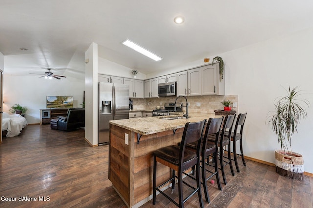 8562 N Audubon Dr, Hayden, ID 83835 - kitchen with appliances with stainless steel finishes, a peninsula, vaulted ceiling, decorative backsplash, and dark wood-type flooring