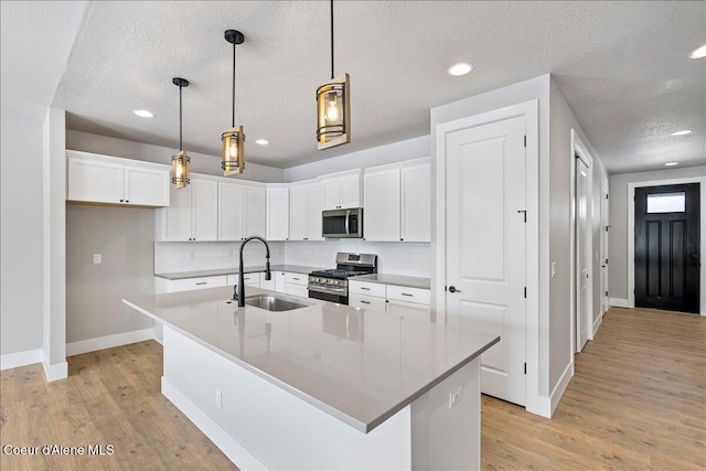 3510 N Cyprus Fox Loop, Post Falls, ID 83854 - kitchen with stainless steel appliances, light wood-style floors, white cabinets, backsplash, and a center island with sink