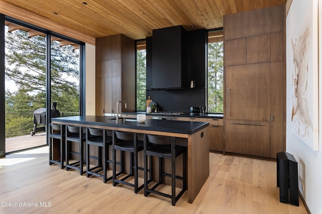 5 Crystal Springs Ct, Sandpoint, ID 83864 - kitchen with dark countertops, a breakfast bar, a center island with sink, wooden ceiling, and light wood finished floors