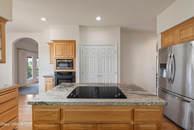 182 Sunnyside Rd, Sandpoint, ID 83864 - kitchen featuring black appliances, arched walkways, light stone counters, light wood-style floors, and a center island