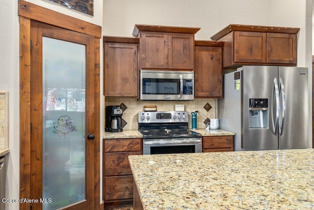 695 W Keva Ln, Athol, ID 83801 - kitchen with stainless steel appliances, decorative backsplash, light stone countertops, and brown cabinetry