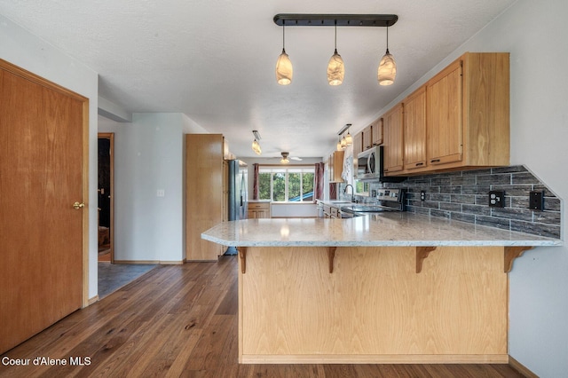 9067 W Coeur D Alene Dr, Spirit Lake, ID 83869 - kitchen with stainless steel appliances, a peninsula, tasteful backsplash, dark wood-style flooring, and light stone counters