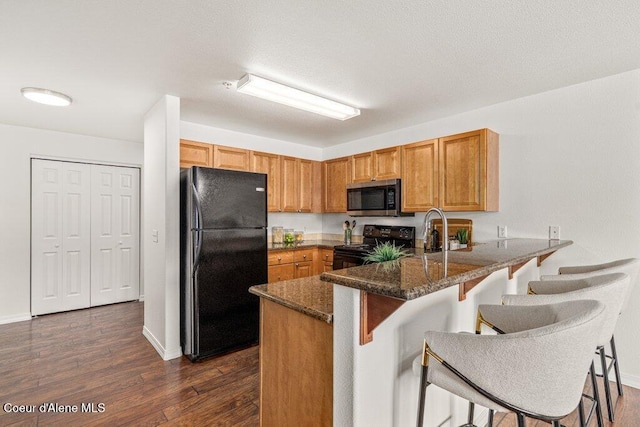 310 N Promenade Loop # 210, Post Falls, ID 83854 - kitchen with black appliances, a peninsula, dark stone countertops, a kitchen breakfast bar, and dark wood-style floors