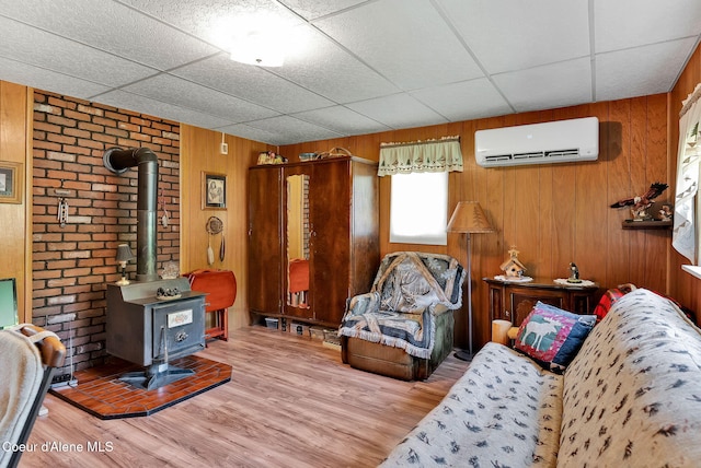 498 Lakeview Rd, Bayview, ID 83803 - living room with a wall mounted AC, a wood stove, wood finished floors, wood walls, and a paneled ceiling