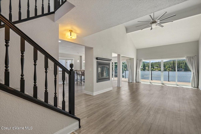 1922 E Rodkey Dr, Post Falls, ID 83854 - unfurnished living room with high vaulted ceiling, a ceiling fan, stairs, wood finished floors, and a water view