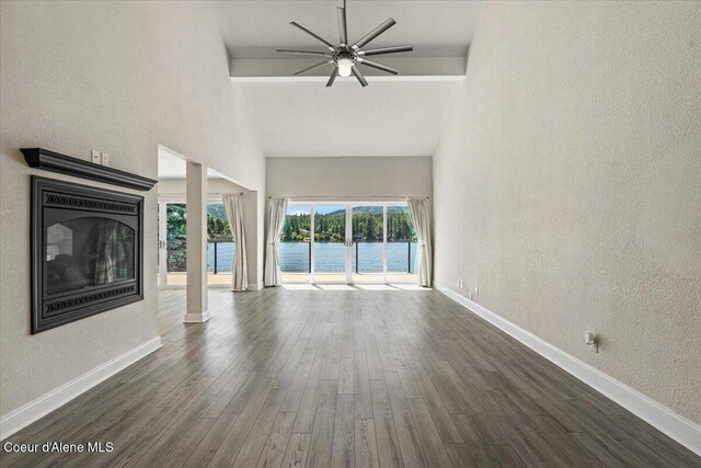 1922 E Rodkey Dr, Post Falls, ID 83854 - unfurnished living room with a textured wall, a ceiling fan, a water view, high vaulted ceiling, and dark wood-style floors