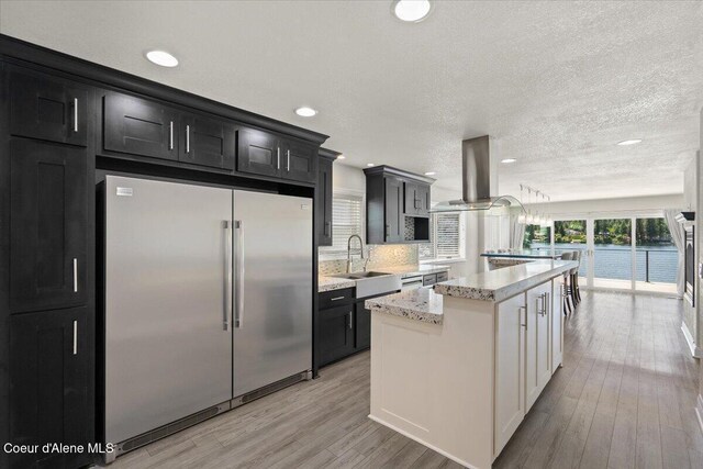 1922 E Rodkey Dr, Post Falls, ID 83854 - kitchen with stainless steel built in fridge, a center island, light wood-style floors, tasteful backsplash, and dark cabinets