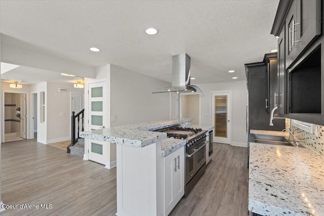 1922 E Rodkey Dr, Post Falls, ID 83854 - kitchen with island range hood, range with two ovens, a kitchen island, light wood-type flooring, and light stone counters
