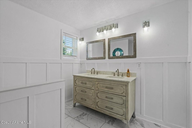 1922 E Rodkey Dr, Post Falls, ID 83854 - bathroom with a decorative wall, marble finish flooring, a textured ceiling, double vanity, and a wainscoted wall