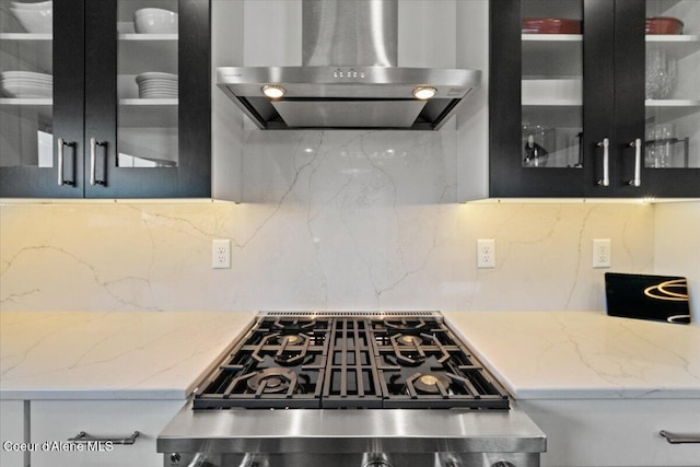 3811 N Foxtail Rd, Post Falls, ID 83854 - kitchen with wall chimney exhaust hood, stove, glass insert cabinets, tasteful backsplash, and light stone countertops