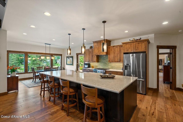 11667 N Eastshore Dr, Hayden, ID 83835 - kitchen with stainless steel refrigerator with ice dispenser, brown cabinetry, wood-type flooring, backsplash, and recessed lighting