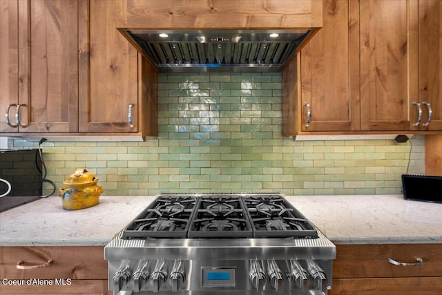 11667 N Eastshore Dr, Hayden, ID 83835 - kitchen featuring range hood, stainless steel gas range, decorative backsplash, brown cabinetry, and light stone countertops