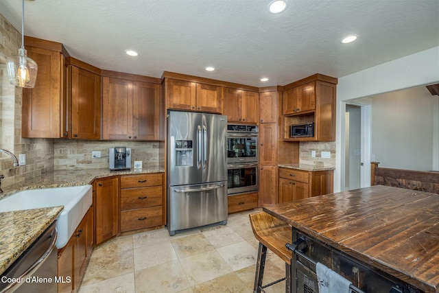 8718 W Sausser Dr, Coeur Dalene, ID 83814 - kitchen featuring appliances with stainless steel finishes, brown cabinetry, decorative backsplash, light stone countertops, and recessed lighting