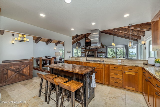 8718 W Sausser Dr, Coeur Dalene, ID 83814 - kitchen with island range hood, stainless steel gas cooktop, light stone counters, brown cabinets, and decorative light fixtures