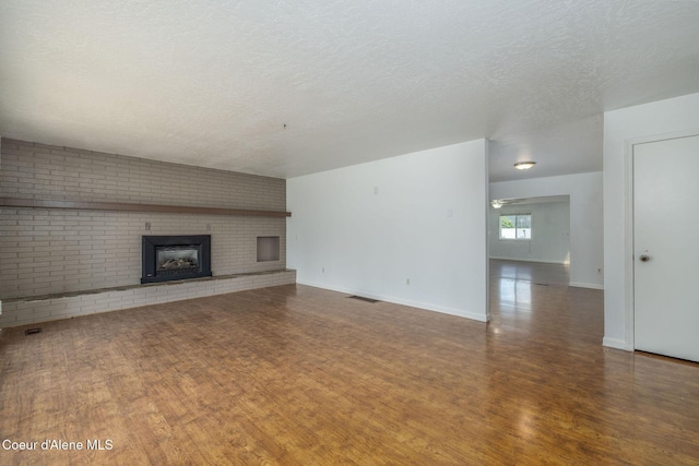 6300 N Sunrise Ter, Coeur Dalene, ID 83815 - unfurnished living room featuring wood finished floors, a brick fireplace, a textured ceiling, and brick wall