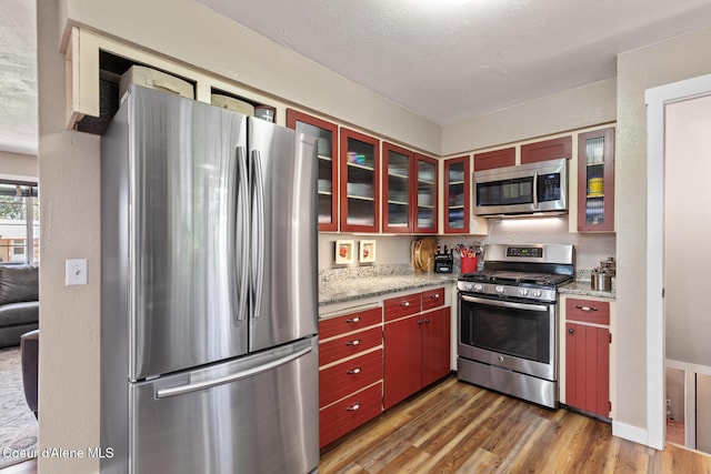 709 E 14th Ave, Post Falls, ID 83854 - kitchen with stainless steel appliances, wood finished floors, red cabinetry, and glass insert cabinets