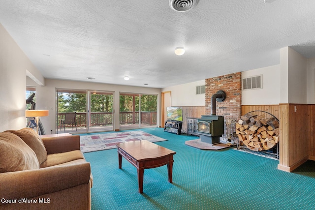 7722 W Clemetson Rd, Coeur Dalene, ID 83814 - living area with a wood stove, wood walls, carpet, a wainscoted wall, and a textured ceiling