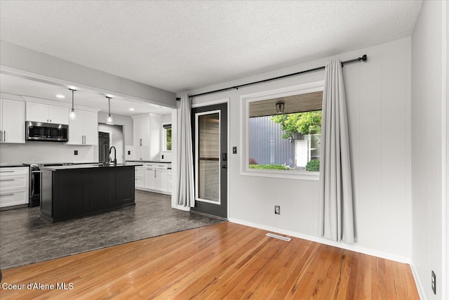 502 W 14th Ave, Post Falls, ID 83854 - kitchen with stainless steel microwave, light wood-style flooring, white cabinetry, a textured ceiling, and a kitchen island with sink