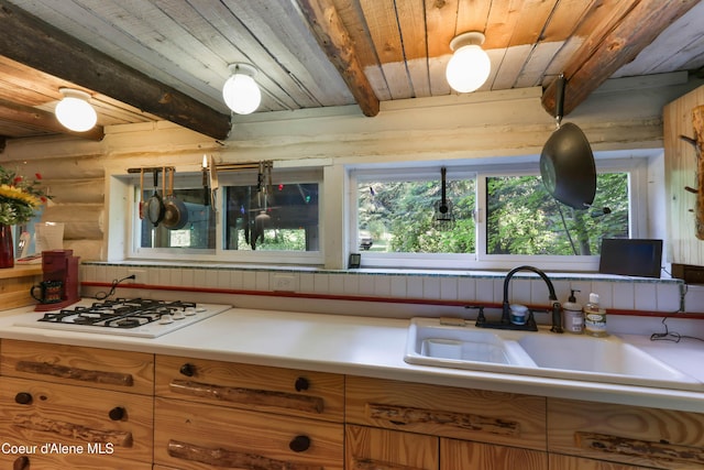 1283 N Wrenco Rd, Sandpoint, ID 83864 - kitchen featuring white gas stovetop, a wooden ceiling with exposed beams, log walls, light countertops, and brown cabinetry