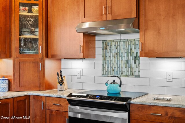 4127 Sagle Rd, Sagle, ID 83860 - kitchen featuring stainless steel range with electric cooktop, ventilation hood, backsplash, glass insert cabinets, and brown cabinets