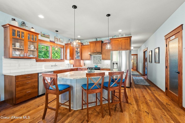 4127 Sagle Rd, Sagle, ID 83860 - kitchen with appliances with stainless steel finishes, brown cabinetry, under cabinet range hood, backsplash, and dark wood finished floors