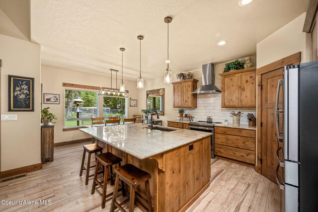 21315 N Eclipse Rd, Rathdrum, ID 83858 - kitchen with appliances with stainless steel finishes, wall chimney exhaust hood, light wood finished floors, backsplash, and an island with sink
