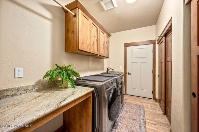 21315 N Eclipse Rd, Rathdrum, ID 83858 - washroom with washing machine and dryer, cabinet space, light wood-style flooring, a textured wall, and a textured ceiling