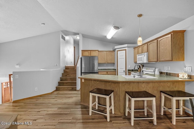 5735 E Steamboat Bnd, Post Falls, ID 83854 - kitchen with vaulted ceiling, a peninsula, white microwave, a kitchen bar, and light wood finished floors