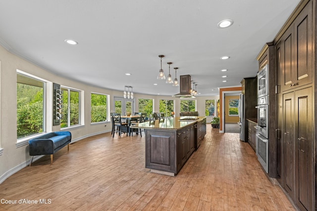 822 Ridgewood, Kamiah, ID 83536 - kitchen featuring range hood, dark brown cabinetry, recessed lighting, an island with sink, and pendant lighting