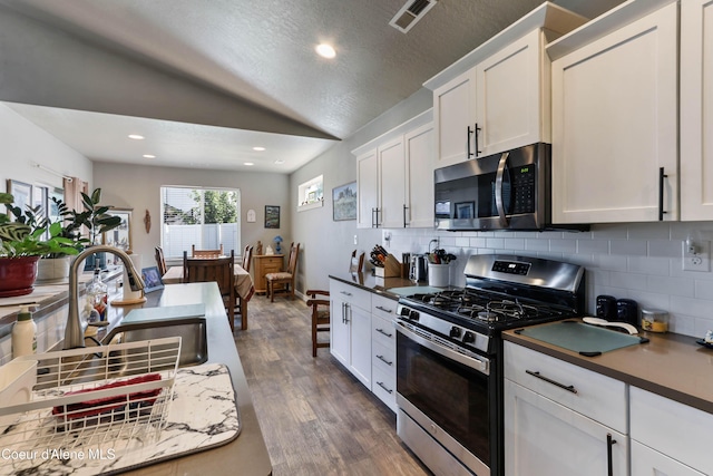 4574 N Connery Loop, Post Falls, ID 83854 - kitchen featuring stainless steel appliances, lofted ceiling, backsplash, white cabinetry, and dark wood-style floors