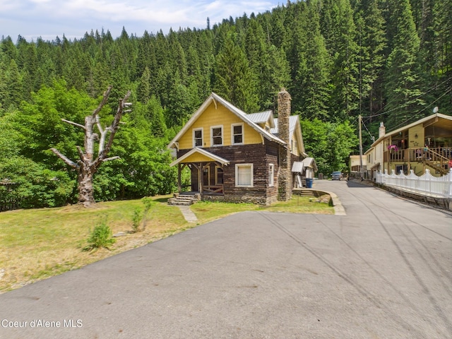 185 King St, Wallace, ID 83873 - view of front facade featuring a wooded view, stone siding, a front lawn, a porch, and a chimney