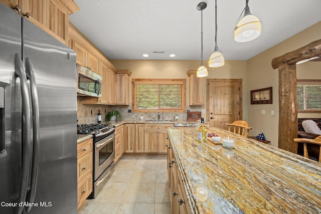 1911 Carr Creek Rd, Sandpoint, ID 83864 - kitchen featuring stainless steel appliances, light brown cabinetry, tasteful backsplash, light stone counters, and hanging light fixtures