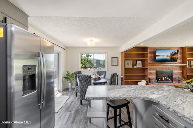 1024 W Mill Ave, Coeur Dalene, ID 83814 - kitchen with stainless steel refrigerator with ice dispenser, a textured ceiling, light wood-style flooring, a breakfast bar, and a fireplace