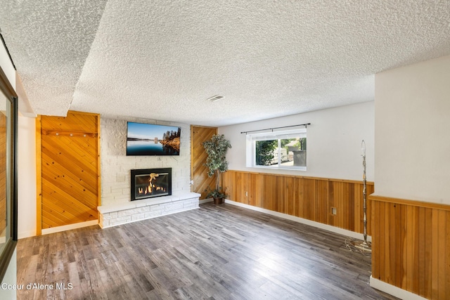 1024 W Mill Ave, Coeur Dalene, ID 83814 - unfurnished living room featuring wood walls, a large fireplace, wood finished floors, a textured ceiling, and wainscoting
