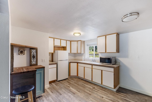 1024 W Mill Ave, Coeur Dalene, ID 83814 - kitchen featuring freestanding refrigerator, stainless steel microwave, light wood-style floors, and white cabinets