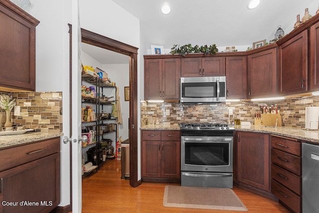 6487 W Covenant St, Rathdrum, ID 83858 - kitchen featuring appliances with stainless steel finishes, light wood finished floors, decorative backsplash, recessed lighting, and light stone countertops