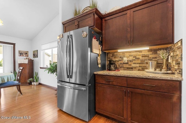 6487 W Covenant St, Rathdrum, ID 83858 - kitchen featuring freestanding refrigerator, vaulted ceiling, tasteful backsplash, light wood-type flooring, and light stone counters