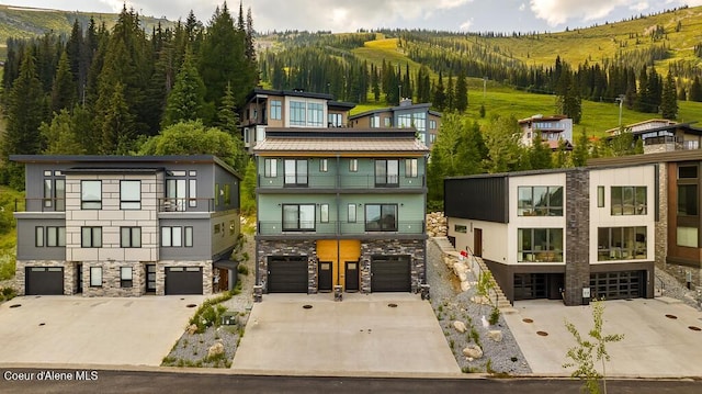 98 Chutes Ln, Sandpoint, ID 83864 - view of front of house featuring stone siding, a balcony, a forest view, driveway, and a garage