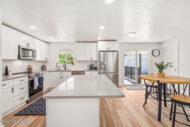320 E Dakota Ave, Hayden, ID 83835 - kitchen with appliances with stainless steel finishes, a center island, backsplash, light wood-style floors, and a textured ceiling